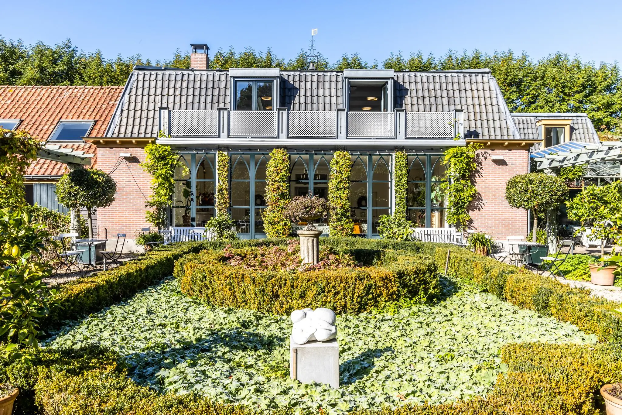 Sfeervolle tuin met buxushagen en kunstwerk voor een charmante woning aan de Langbroekerdijk.